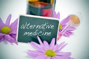 Small chalkboard with "alternative medicine" text surrounded by purple flowers and colorful glass bottles