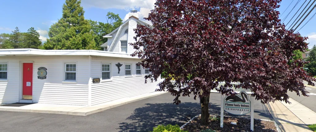 White single-story building with red door and dark red foliage tree in front